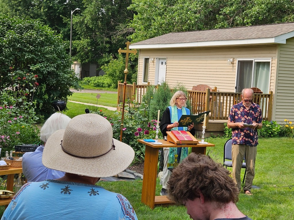 Priest at outdoor church service in front of flowers.