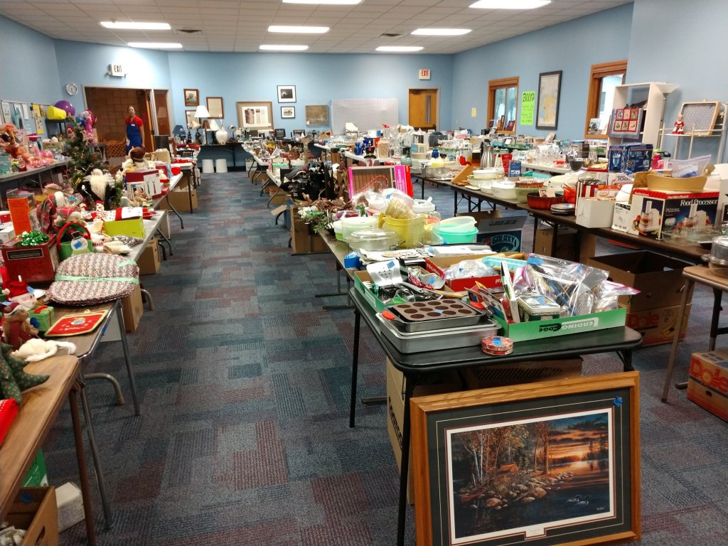 Photo of long tables filled with items for sale in Parish Hall. 