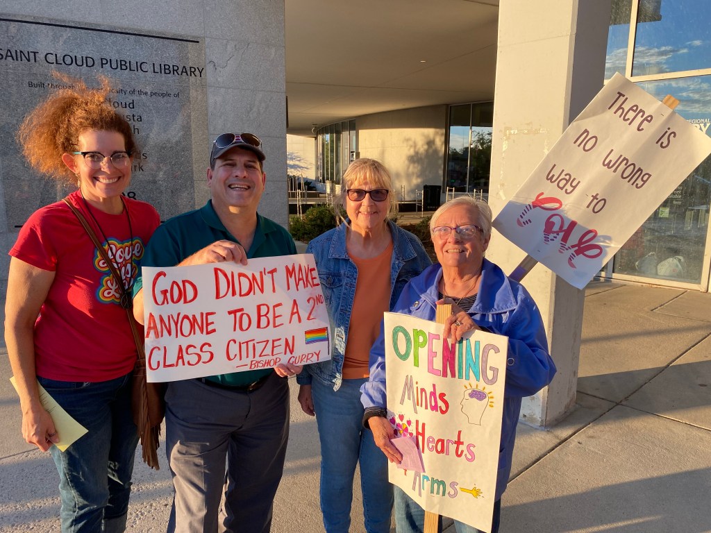 Four church members holding up LGBT Pride flags in pride parade.